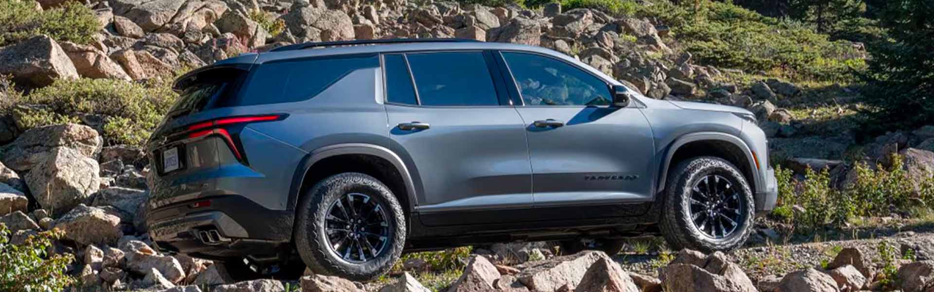 2025 Chevrolet Traverse SUV driving off-road on rocky terrain, showcasing rugged tires, modern gray exterior, and adventure-ready design.