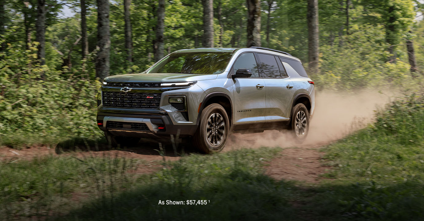 2026 Chevy Traverse gray midsize SUV driving off-road through a forest trail with dust behind it