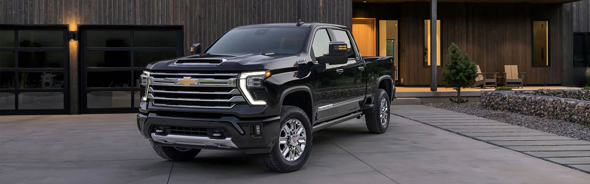 2026 Chevrolet Silverado HD in black parked outside a modern home with illuminated garage doors.
