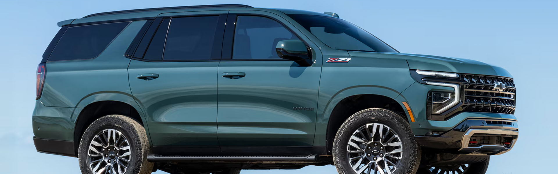 2026 Chevrolet Tahoe Z71 full-size SUV in green, shown in side profile with off-road styling, black wheels, and chrome grille against a clear blue sky.